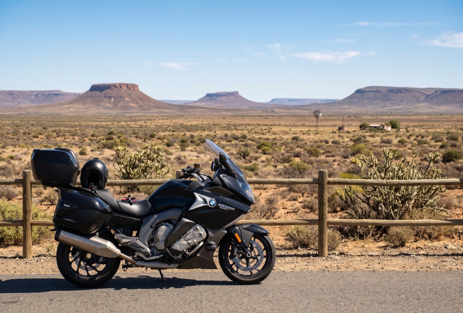 A black BMW K1600 grand tourer parked on a quiet road in the Great Karoo, with flat-topped koppies and a windmill on the horizon.