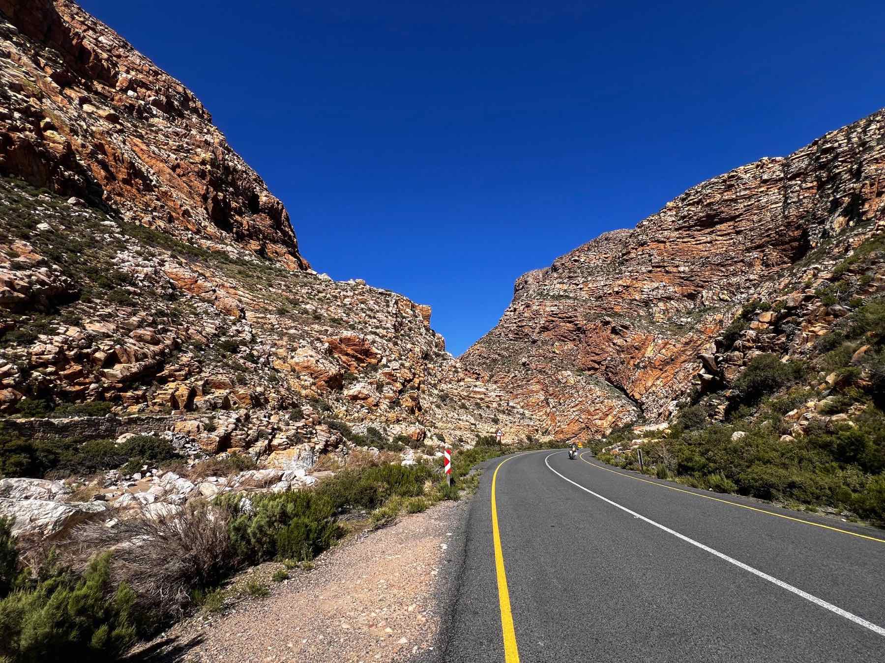 A rider on a touring motorcycle threading the towering rock walls of Meiringspoort.